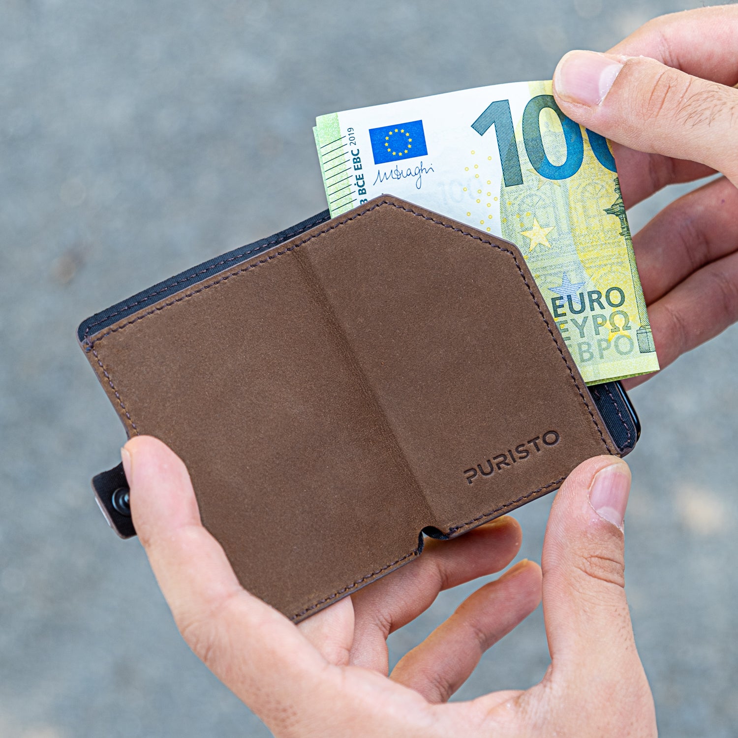 Due mani tengono un portagoglio in mano, la mano destra sfila una banconota da 100€. Sfonfo chiaro.