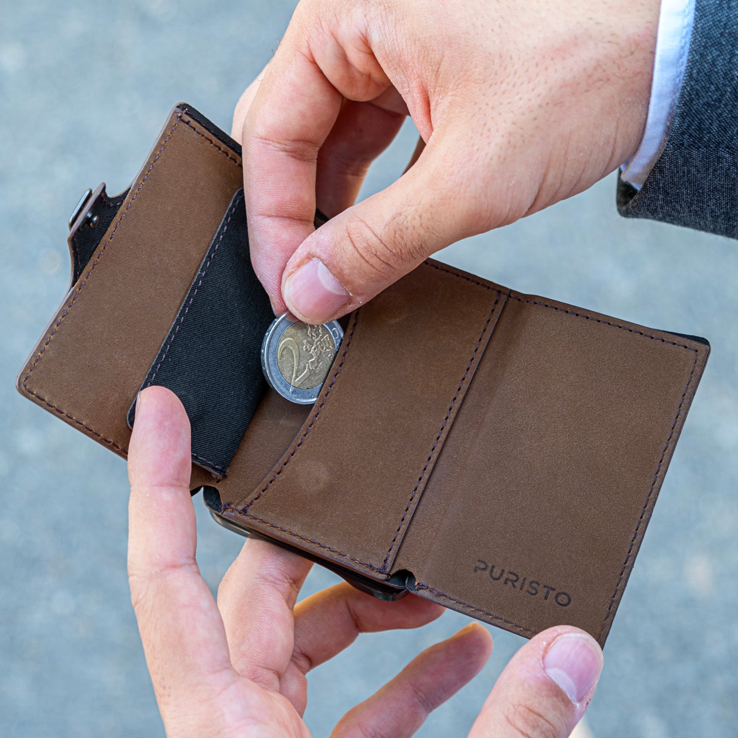 Due mani tengono un portafoglio, la mano destra sfila una moneta da 2 euro. Sfondo chiaro.