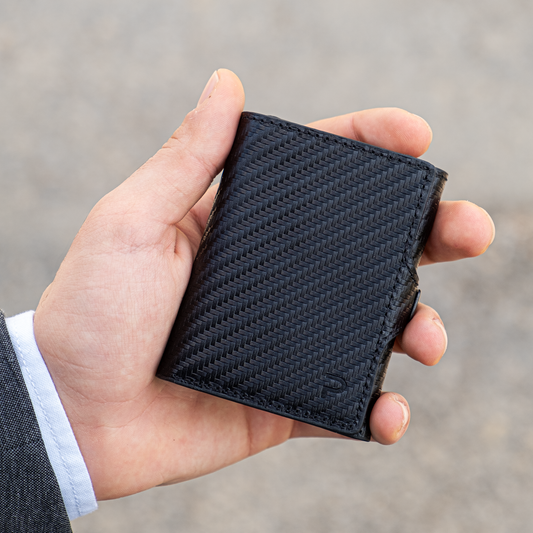 Mano tiene un portafoglio nero carbon elegante. Sfondo chiaro