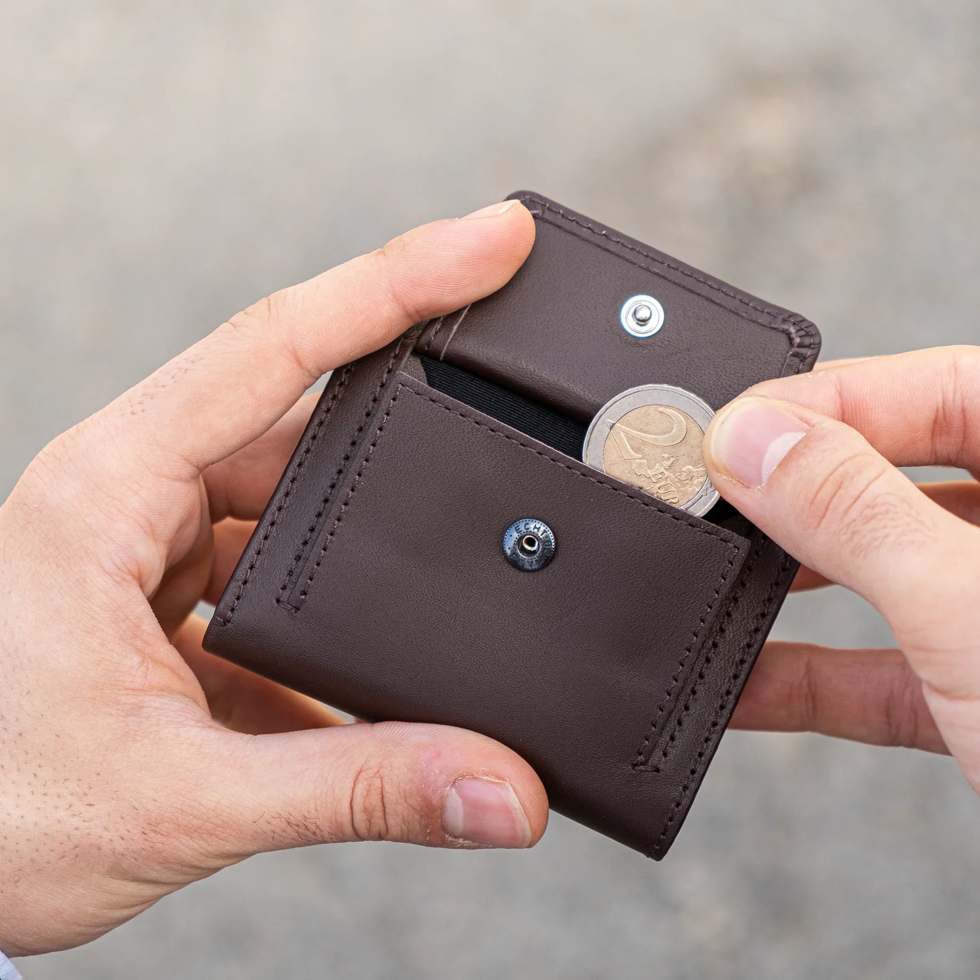 Miniwallet marrone con portamonete, mani che inseriscono una moneta da due euro