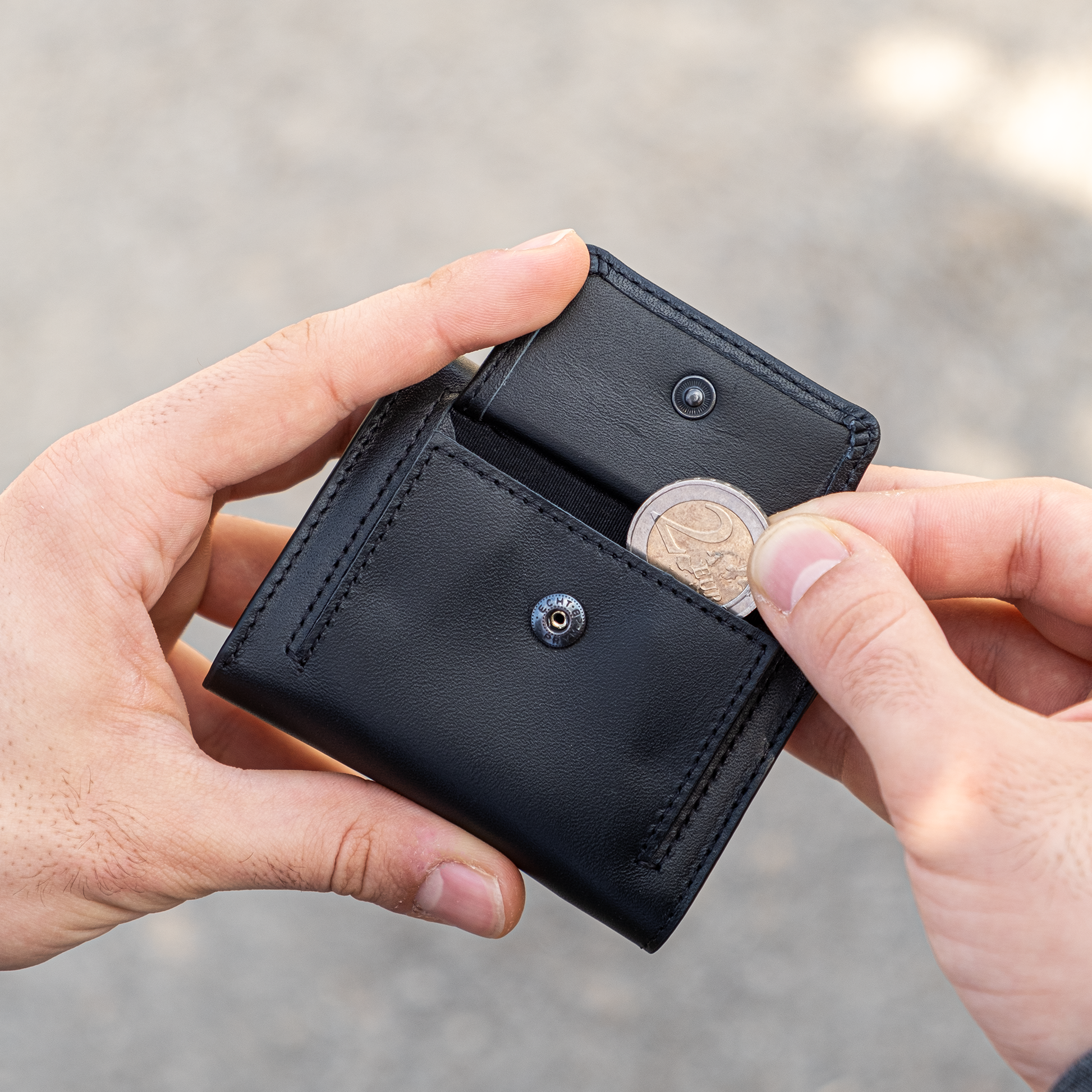 Due mani tengono un portamonete in mano , la destra estrae una moneta da 2 euro. Sfondo chiaro