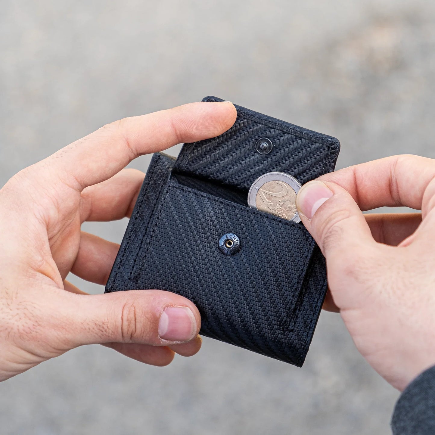 Miniwallet nero compatto con portamonete, tenuto in mano mentre si inserisce una moneta euro.
