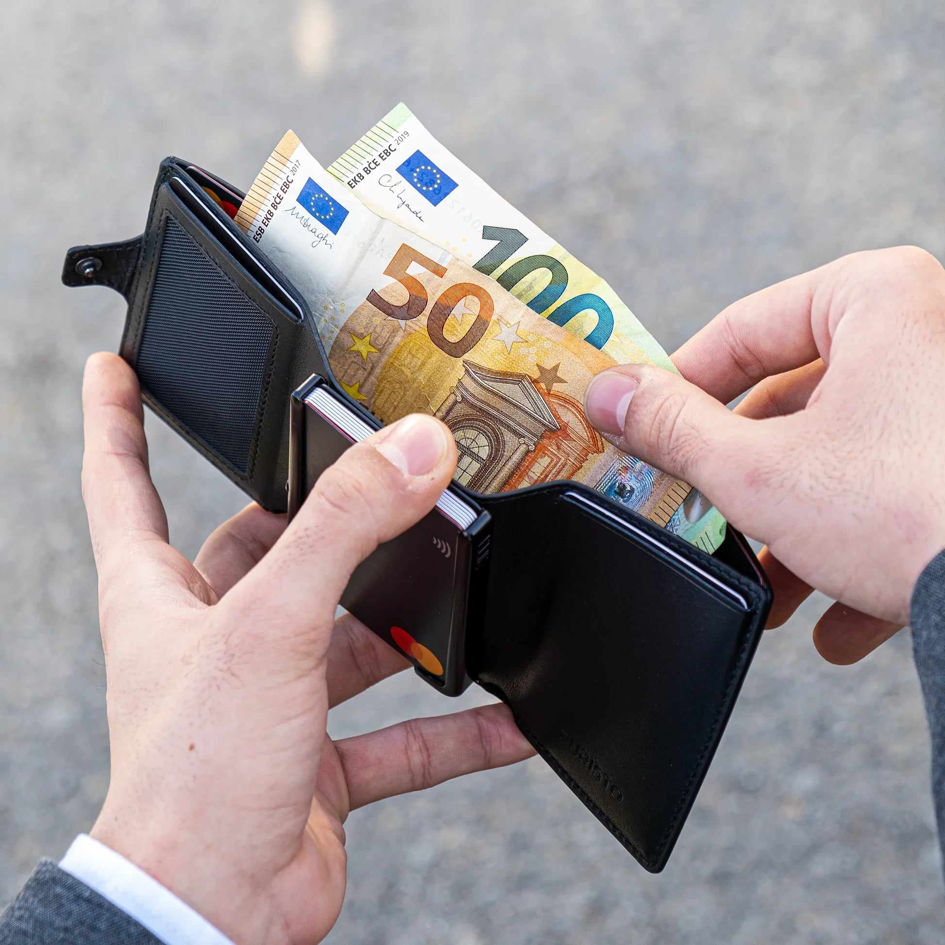 Miniwallet nero compatto aperto, con banconote euro e carte di credito visibili in mano