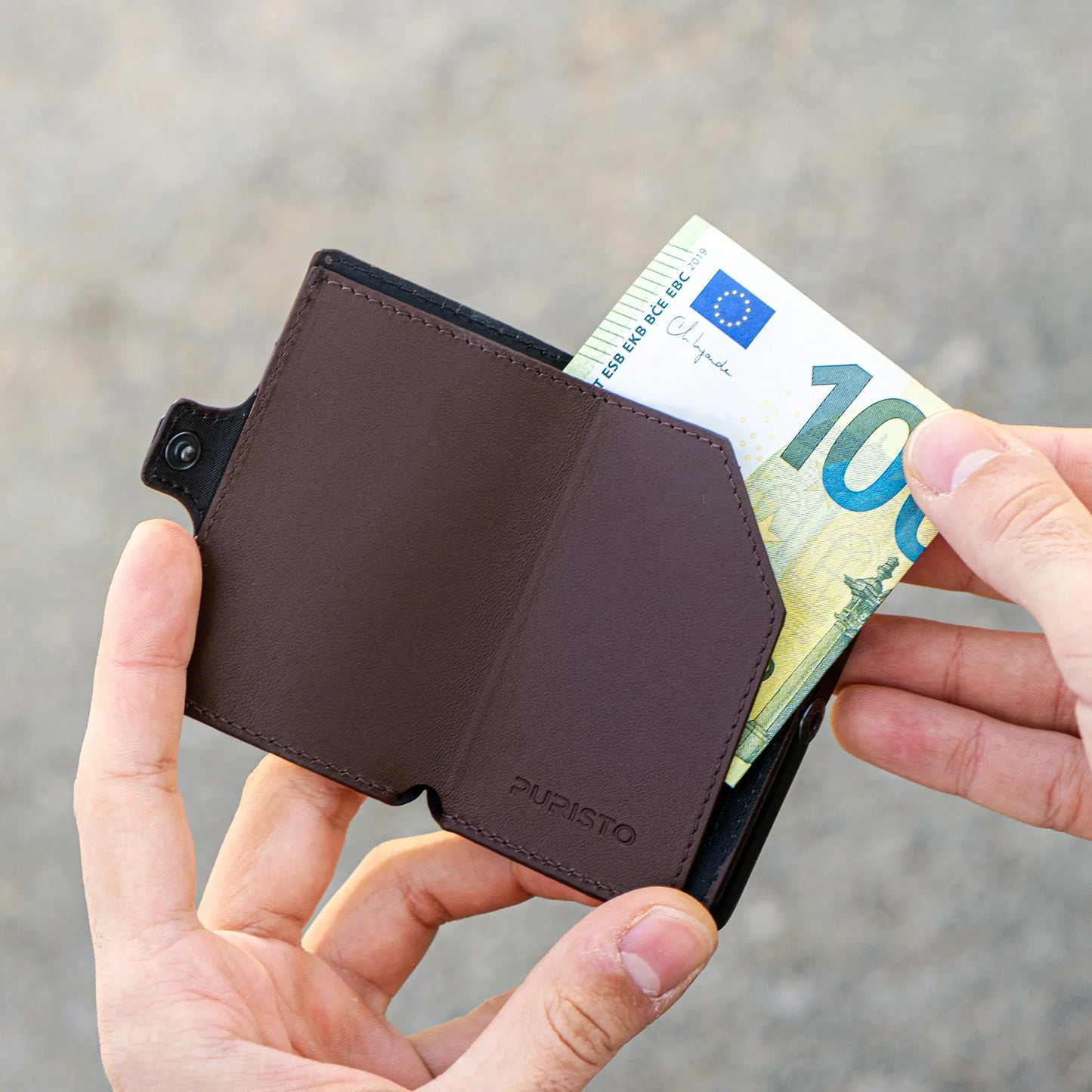 Miniwallet marrone compatto con banconota da 100 euro, portafoglio slim in mano