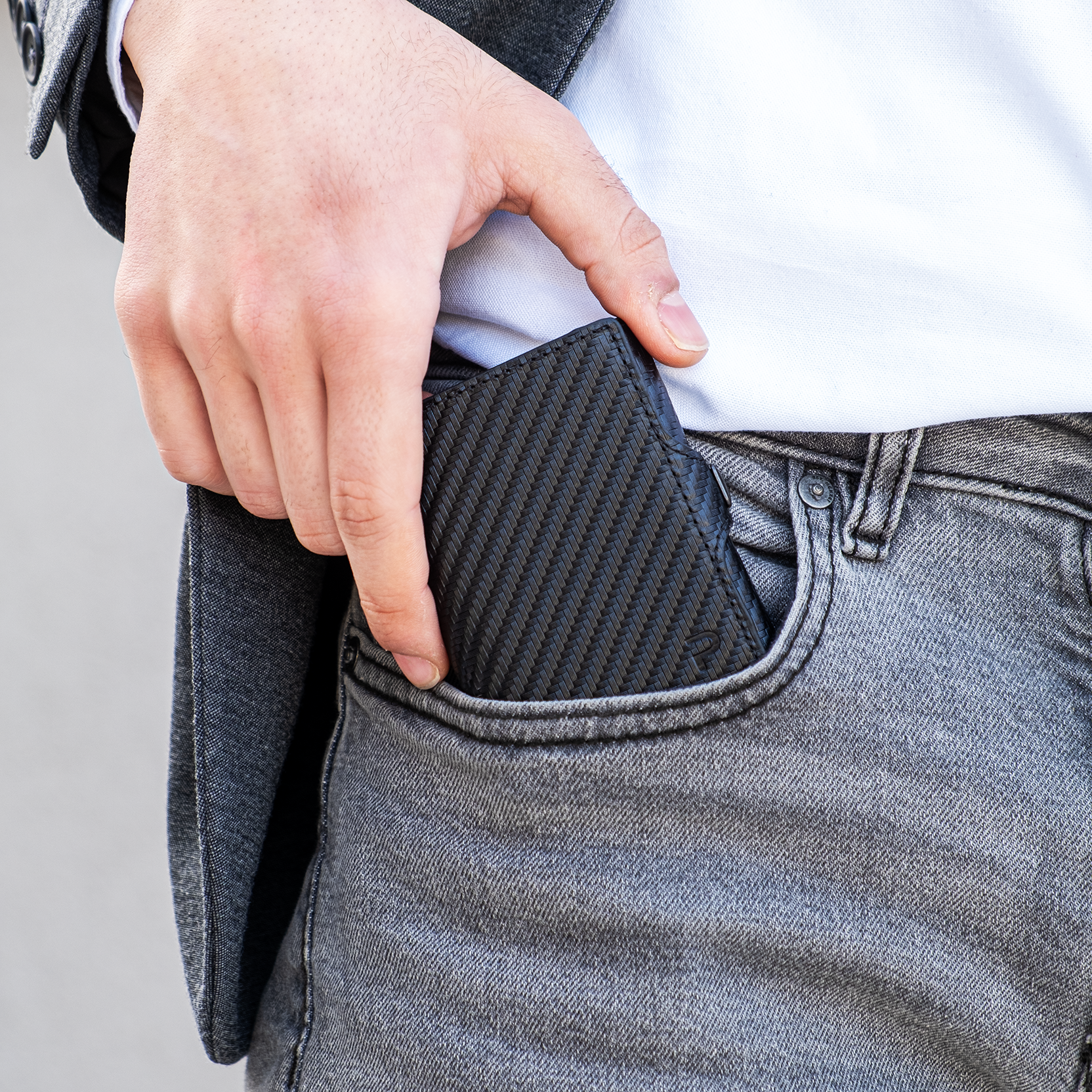Mano estrae portafoglio nero in carbon dalla tasca anteriore dei pantaloni. Sfondo elegante