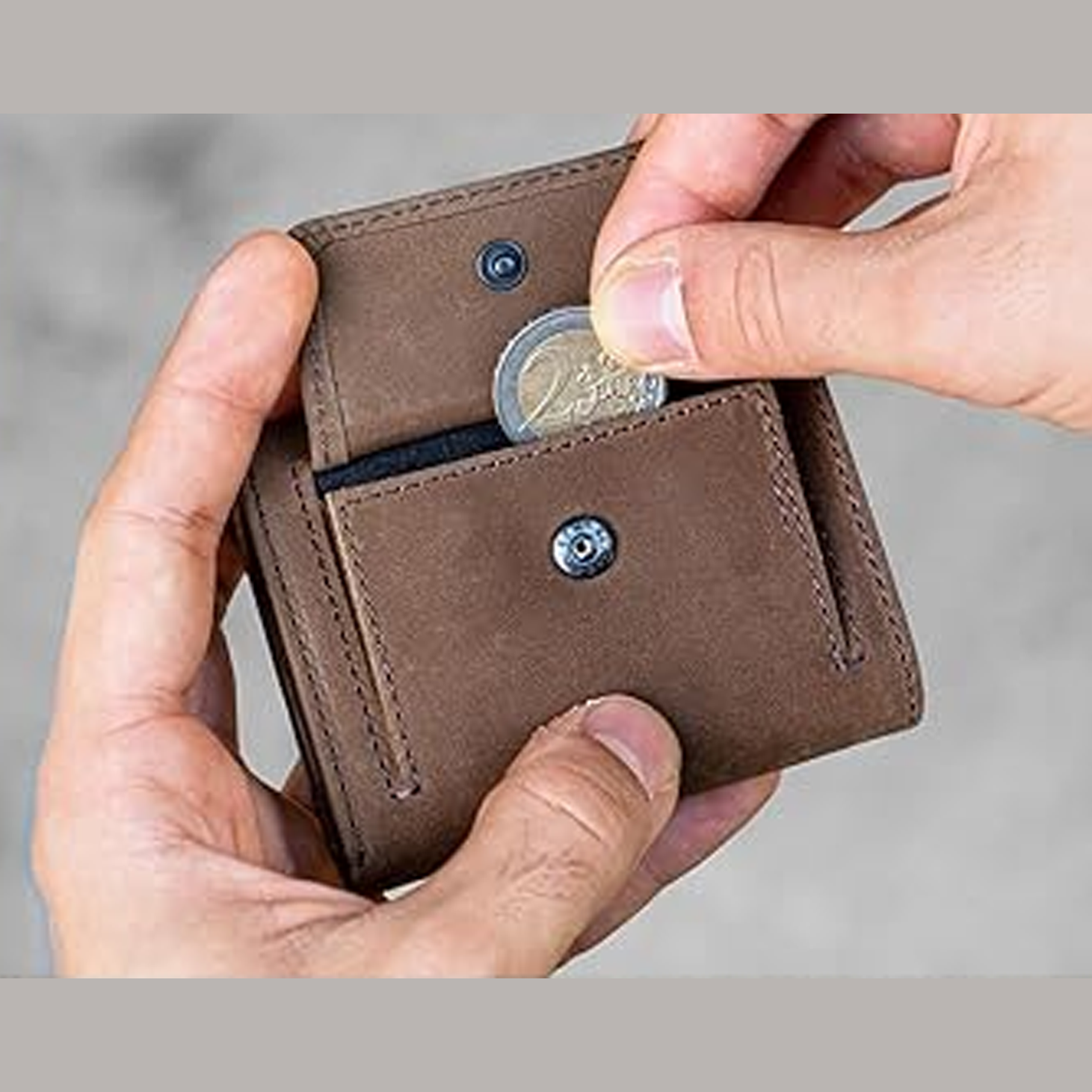 Due mani tengono un portamonete in mano , la destra estrae una moneta da 2 euro. Sfondo chiaro