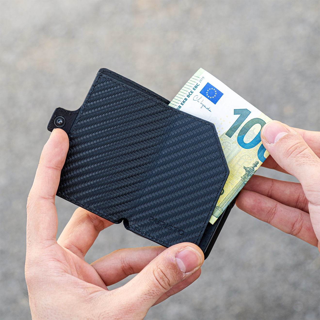 Due mani tengono un portagoglio in mano, la mano destra sfila una banconota da 100€. Sfonfo chiaro.