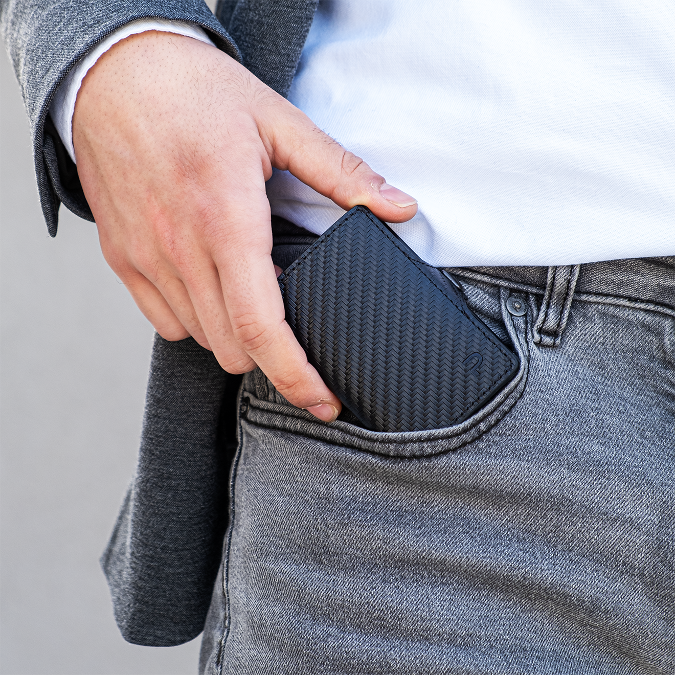 Mano sfila portafoglio slim dalla tasca frontale dei pantaloni. Sfondo elegante in jeans.