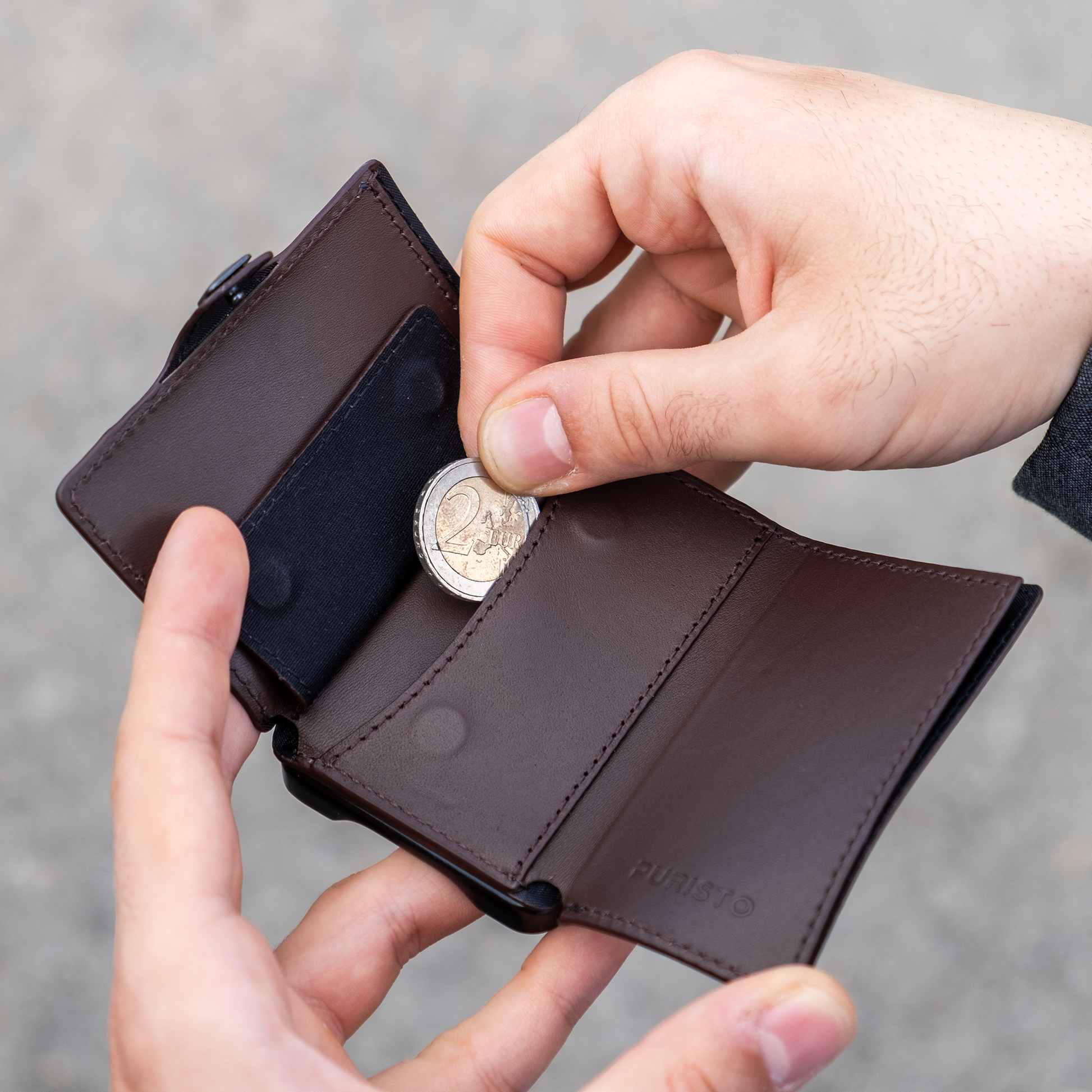 Due mani tengono un portafoglio, la mano destra sfila una moneta da 2 euro. Sfondo chiaro.
