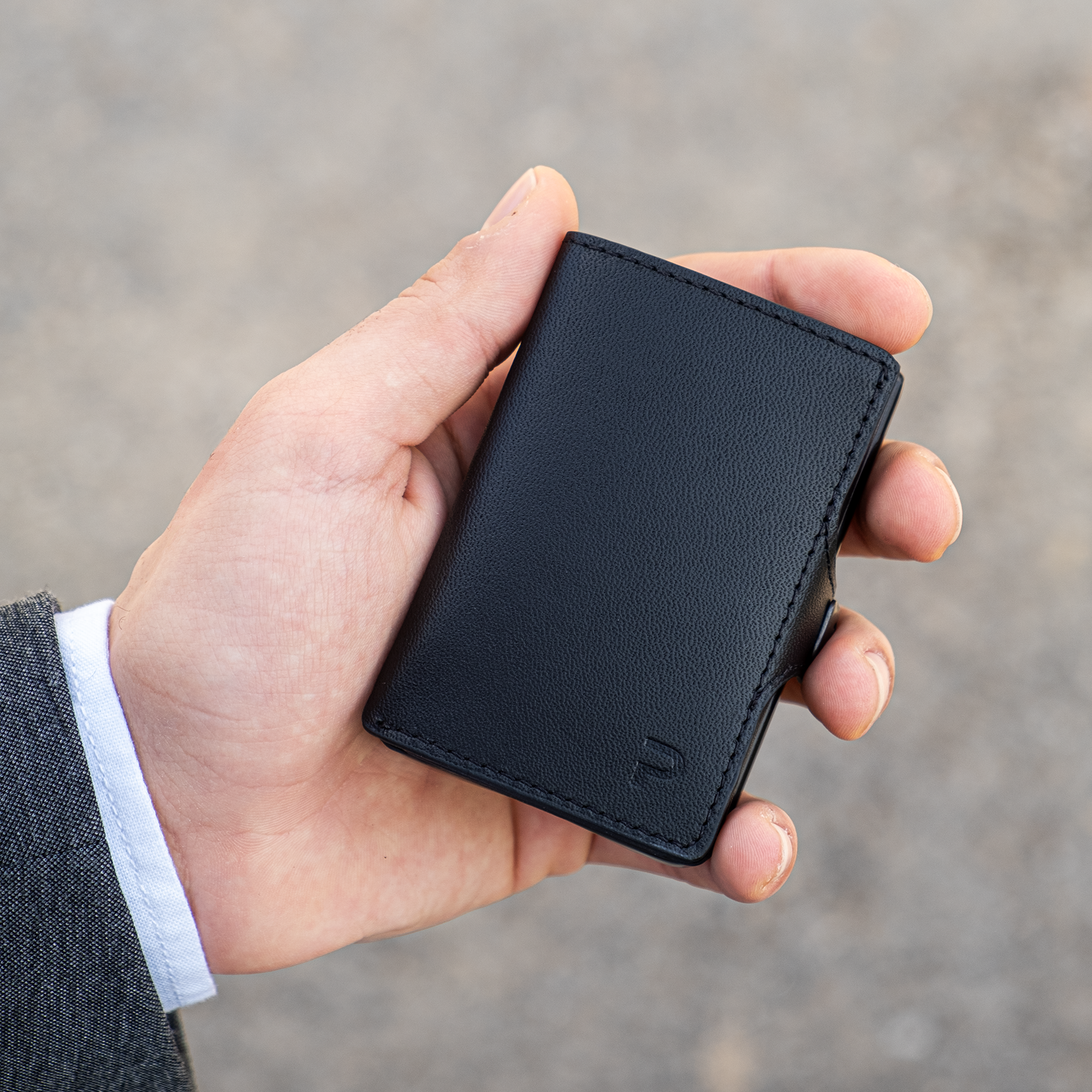 Mano tiene un portafoglio nero in materiale Mirum elegante. Sfondo chiaro